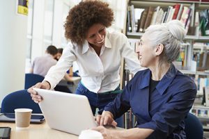 Teacher Helping Mature Student With Studies In Library-Personal Enrichment